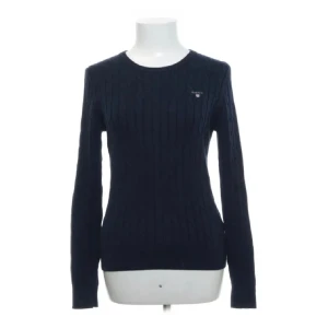 Marinblå stickad tröja GANT - Snygg marinblå tröja från GANT med diskret logga på bröstet. Stretchig bomullskvalitet och rund halsringning. Långärmad och slim passform som sitter riktigt bra. Perfekt för dig som gillar klassisk och stilren look.