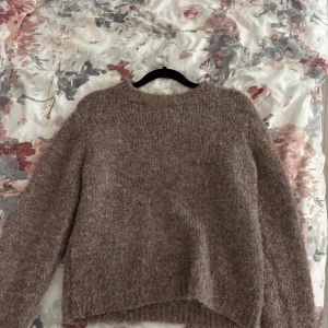 Beige fluffig stickad tröja - Mysig och fluffig stickad tröja i brun ton med rund hals och långa ärmar. Perfekt för kyliga dagar och har en enkel, stilren design som är lätt att matcha med jeans eller kjol. Tröjan har en mjuk och skön känsla som gör den superbekväm att bära. Andvönd 1 gång 