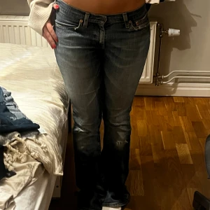 Levi's 514 bootcut jeans blå - Säljer ett par klassiska Levi's 514 jeans i blå tvätt med bootcut passform. Jeansen har låg midja, slitningar och lätt urtvättade detaljer för en cool vintagekänsla. Tillverkade i robust denim med fem fickor och dragkedjegylf. De har ett hål i rumpan där av priset 