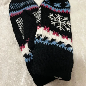 Tre par stickade tumvantar med mönster - Tre par stickade tumvantar i olika färger och mönster. Ett par är svart med vita, blå och röda detaljer och snöflinga, ett par är rosa med hjärtan och blått, och ett par är lila med vita och rosa inslag. Perfekta för kalla vinterdagar och riktigt mysiga. Stlk M-L 79kr/par 