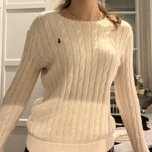 Stickad creme tröja från Polo Ralph Lauren, S - Säljer en klassisk kabelstickad tröja från Polo Ralph Lauren 🤎 Beige med blå broderad logga på bröstet – rund hals, långa ärmar och ribbade kanter. En riktig preppy favorit som alltid funkar, tidlös och supersnygg i garderoben 