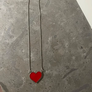 Halsband med rött hjärta - Snyggt halsband med en tunn silverfärgad kedja och ett stort rött hjärta som hänge. Hjärtat har en blank yta och är infattat i silverfärgad metall. Pris kan diskuteras🙏