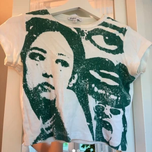 Vit t-shirt med grönt tryck från Subdued - Cool vit t-shirt från Subdued med ett stort grönt grafiskt tryck av ansikten på framsidan. T-shirten har korta ärmar och rund halsringning. 