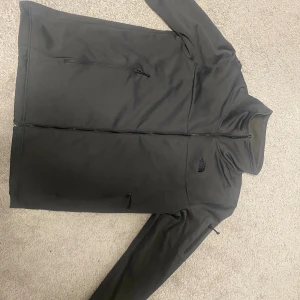 Svart vindjacka från The North Face XL - Svart vindjacka från The North Face i storlek XL. Jackan har hög krage, hel dragkedja framtill och flera praktiska fickor med dragkedja. Materialet är mjukt och känns som syntet/fleece, perfekt för kyliga dagar. Diskret logga broderad på bröstet. PRIS KAN DISKUTERAS VID SNABBAFFÄR 