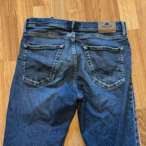 Blå jeans Replay Thad 14A - Snygga blå jeans från Replay, modell Thad. Klassisk femficksdesign med raka ben och normal passform. Jeansen har tydliga kontrastsömmar och Replay-logga på bakfickan samt läderpatch i midjan. Perfekta för dig som gillar stilrena och tidlösa jeans.
