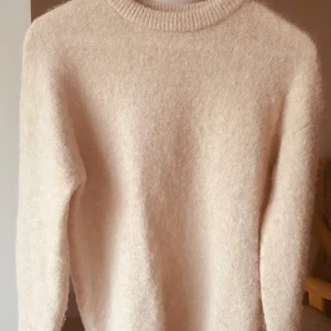 Beige alpaca blend stickad tröja med rund hals - Mysig beige stickad tröja med rundad hals och långa ärmar. Tröjan har en enkel och clean look, perfekt för dig som gillar neutrala färger och vill ha något som är både skönt och stilrent. Passar dig som gillar en klassisk vibe.