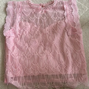 Rosa spetsblus med volangärmar - Säljer en ljusrosa blus med genombruten spets och snygga volangdetaljer på ärmarna. Blusen har ett unikt mönster och rund hals med dekorativa ringar. Ryggen är typ genomskinlig. Kan visa baksidan av tröjan om du är intresserad. 