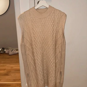 Beigefärgad kabelstickad väst - Beige kabelstickad väst från HM, går ner till mitten av låren på mig som är 169 cm. Storlek M. Slits på båda sidorna. Använd 1-2 gånger och är därmed i mycket bra skick och inga synliga skavanker.