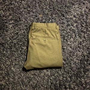 Svarta kostymbyxor J.Lindeberg slim fit - Snygga gröna kostymbyxor från J.Lindeberg i slim fit-modell. Byxorna är tillverkade i 100% ull och har en bakficka med knapp. Perfekta för dig som gillar en stilren och modern look.