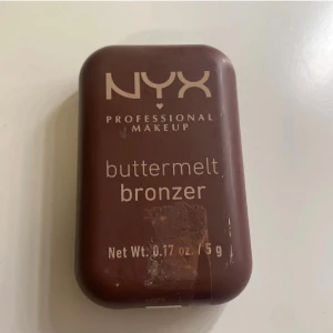 NYX buttermelt bronzer - NYX buttermelt bronzer i en kompakt brun förpackning. Pudret har en varm brun nyans med lätt skimrande finish och vågigt mönster i ytan. Perfekt för att skapa en solkysst look och definiera ansiktskonturer.