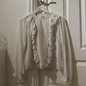Vit blus med volanger från Gina Tricot - Supersöt vit blus från Gina Tricot med volangdetaljer längs framsidan och ärmsluten. 💞