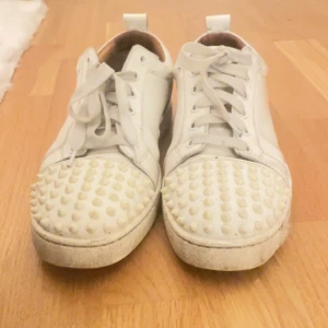 Christian Louboutin vita sneakers med nitar - Säljer ett par vita sneakers från Christian Louboutin med röd sula & nitar. Billiga då jag säljer för dem är utslitna!