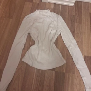 Vit ribbad polotröja Gina Tricot - Säljer en vit ribbad polotröja från Gina Tricot i storlek M. Tröjan har lång ärm, smal passform och en hög krage som ger en clean och stilren look. Perfekt att styla med jeans eller kjol för en enkel men snygg outfit.