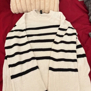 Vit och svart randig stickad tröja - Säljer en vit stickad tröja med svarta horisontella ränder. Tröjan har rund hals och långa ärmar med breda ribbade muddar vid ärmslut och nederkant. Perfekt för dig som gillar klassisk och chill stil.