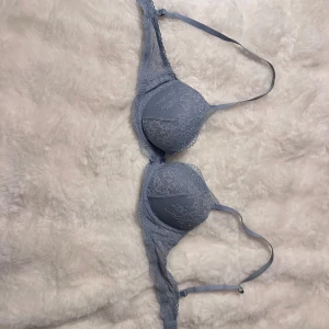 Blå spets-bh från H&M 75A - Säljer en ljusblå bh från H&M i storlek 75A. Bh:n har fina spetsdetaljer på kuporna och sidorna samt justerbara axelband. Utsidan är i spets och insidan är slät och mjuk. Materialet är en mix av polyamid och elastan.