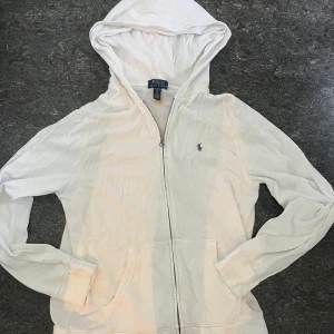 Vit Polo Ralph Lauren zip - Vit hoodie från Polo Ralph Lauren i storlek S. Klassisk design med dragkedja framtill, huva och två fickor. Liten broderad logga på bröstet. Perfekt för en chill och stilren look.