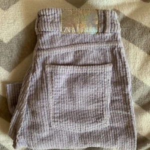 Ljuslila manchesterbyxor från Zara - Säljer ett par ljuslila manchesterbyxor från Zara med raka ben och klassisk femficksdesign. Byxorna har dragkedja och knapp framtill samt en snygg holografisk patch bak i midjan. Perfekta för dig som vill sticka ut med en unik färg och cool retrostil.