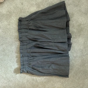 Mörkgrå volangkjol med resår - Supersnygg mörkgrå kjol med volanger och bred resår i midjan. Kjolen har en luftig och skön passform som ger en cool och avslappnad vibe. Perfekt att matcha med en stickad tröja eller t-shirt för en trendig look.