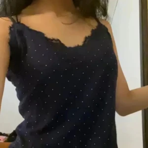 Mörkblå prickig linnetopp med spets - Snygg mörkblå linnetopp med tunna axelband och små vita prickar över hela tyget. Toppen har spetsdetaljer längs urringningen som ger en extra touch. Perfekt för dig som gillar en enkel men ändå söt stil.