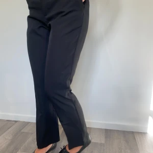 Svarta kostymbyxor från Bik Bok - Svarta kostymbyxor från Bik Bok i klassisk rak modell med hög midja och bälteshällor. Byxorna har diskret dragkedja och knapp framtill, samt raka ben som ger en clean och stilren look. Perfekta till en snygg topp eller skjorta.