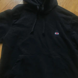 !BUDA, SÄLJER I T-SHIRT OCKSÅ! Svart hoodie med broderad detalj - Svart hoodie med snörning i huvan och en liten broderad detalj på bröstet som ser ut som ett kuvert med röd accent. Klassisk känguruficka framtill och mjukt material, perfekt för chill dagar.