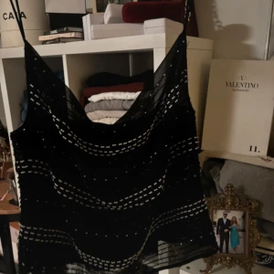 Svart glittrig linnetopp med paljetter - Supersnygg svart linnetopp med tunna axelband och glittriga paljettdetaljer i vågiga rader. Toppen har en lätt transparent känsla och är perfekt för att sticka ut. Sitter snyggt och är enkel att styla till jeans eller kjol.