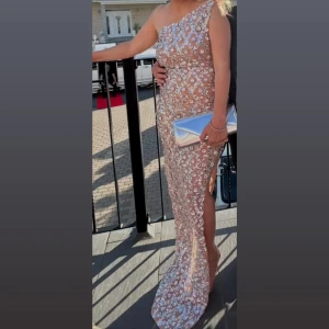 Champagnefärgad långklänning med paljetter - Säljer en elegant champagnefärgad långklänning med glittriga paljetter och blommigt mönster. Klänningen har oneshoulder-design och en slits på sidan som ger en snygg touch. Perfekt för speciella tillfällen när du vill sticka ut. ✨Använd endast en gång. 