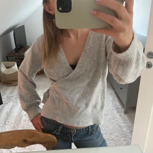 Grå omlottkofta med knyt i sidan - Mysig grå omlottkofta med knyt i sidan och breda ribbade muddar. Koftan är stickad och har lång ärm, perfekt för lager-på-lager under kyliga dagar. Enkel att styla med jeans eller kjol för en chill look. Skriven med AI ahahha skriv om ni har några mer frågor!!❤️❤️säljer jeansen på första bilden också!