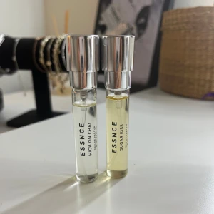 Essnce High on Chai & Sugar Kiss parfym - Två stilrena parfymflaskor från Essnce, High on Chai och Sugar Kiss. Flaskorna är små, cylinderformade med transparent glas och silvriga lock. High on Chai är klar medan Sugar Kiss har en svagt gul ton. Perfekt att ha med i väskan för en fräsch doftboost.