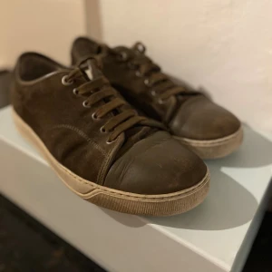Bruna mockasneakers med skinn, Lanvins - Snygga bruna sneakers i mocka med detaljer i skinn på tån och snörning framtill. Skorna har en vit sula med retrovibbar och en klassisk låg profil. Perfekta för dig som gillar stilrena och tidlösa sneakers med en twist. Ett par grymma lanvins, allt og som box kommer med!