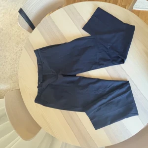 Mörkblå kostymbyxor med wide fit från dressman. Nypris 1400:- - Snygga mörkblå kostymbyxor med rak och vid passform. Byxorna har klassisk midja, knapp och dragkedja framtill. Perfekta för en clean och stilren look. Materialet känns mjukt och följsamt, troligtvis bomull eller polyester.