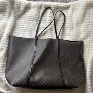 Bag - Snygg och rymlig shoppingväska från H&M i mörkbrunt med diskret rutigt mönster. Väskan har långa svarta axelband och är perfekt för att bära med sig allt man behöver. Insidan är svart med en praktisk innerficka.