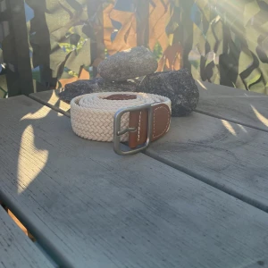 Beige flätat bälte med skinn-detaljer - Snyggt beige flätat bälte med bruna skinn-detaljer vid spännet och en silvrig metallspänne. Bältet har en stilren och enkel design som passar till många olika outfits. Perfekt accessoar för att lyfta din look.
