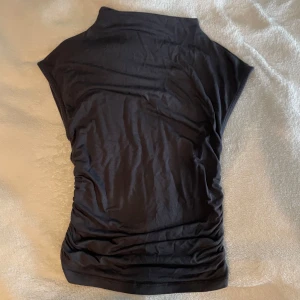 Svart polotopp  - Svart polotopp från Gina Tricot i storlek XS. Toppen har en låg polo hals, har snygg rynkdetalj på sidan. Medela om fler bilder!