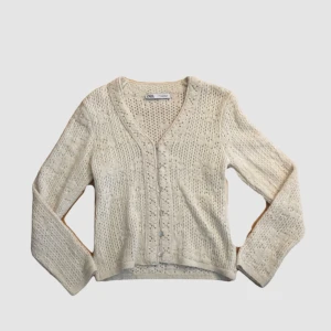 Beige stickad kofta från Zara - Supersöt beige stickad kofta från Zara med v-ringning och fina virkade detaljer. Koftan har långa ärmar, pärlemorknappar framtill och ett luftigt, mönstrat stickat material som ger en romantisk vibe. Perfekt att slänga över en topp eller klänning.