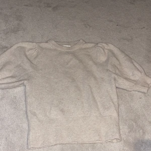 Beige stickad tröja från H&M - Mysig beige stickad tröja från H&M i storlek S. Tröjan har puffiga ärmar och ribbade muddar vid ärmslut och nederkant. Perfekt för lager-på-lager och passar till många olika outfits.