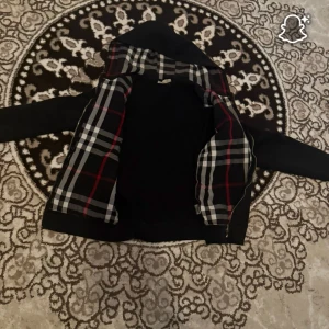 Burberry Hoodie - Svart hoodie från Burberry med klassiskt rutigt foder i huvan och längs insidan. Tröjan har huva med snörning, lång ärm och dragkedja framtill. Perfekt för dig som gillar stilrena designer med en touch av lyx.