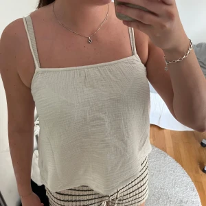 Vit linnetopp med tunna axelband - Säljer en luftig vit linnetopp med tunna axelband och avslappnad passform. Toppen är tillverkad i ett mjukt, strukturerat bomullstyg som känns skönt mot huden. Perfekt för varma dagar och enkel att matcha med olika stilar.