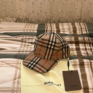 Burberry rutig keps beige M - Snygg Burberry keps i klassiskt rutigt mönster med beige, svart, vit och röd färg. Justerbar baktill med svart plastspänne och Burberry London England-logga. Tillverkad i Italien av bomull. Perfekt för dig som vill ha en ikonisk streetstil. Storlek M!