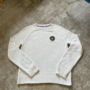 Vit stickad tröja från Ralph Lauren - Vit stickad tröja från Polo Jeans Company by Ralph Lauren. Tröjan har rund halsringning med ribbade muddar och nederkant. På bröstet sitter en broderad patch med Ralph Lauren-logga i blått, rött och vitt. Perfekt för dig som gillar klassisk och clean stil.