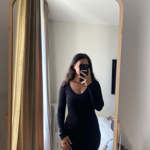 Svart ribbad klänning från Amisu - Säljer en svart, ribbad klänning från Amisu i storlek 36. Klänningen har lång ärm, v-ringad hals och är figurnära med stretchigt stickat material. Perfekt för dig som gillar enkel och stilren look med lite edge.