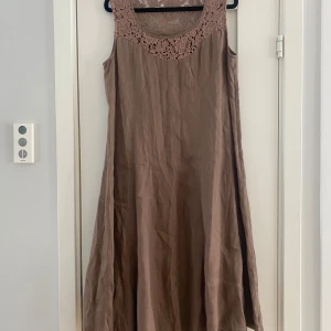 Beige långklänning med spetsdetalj - Säljer en beige långklänning med vacker spets upptill och ärmlös design. Klänningen har en mjuk, flowy passform och är tillverkad i linne. Spetsen har ett blommigt mönster som ger en romantisk vibe. Perfekt för dig som gillar boho-stil och vill ha något luftigt och snyggt.