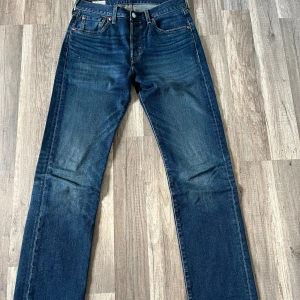 Levi's 501 mörkblå jeans straight fit - Klassiska Levi's 501 jeans i mörkblå tvätt med raka ben och fem fickor. Jeansen har normal passform, knappgylf och snygga slitningar på framsidan. Perfekt för dig som gillar tidlös stil och vill ha ett par jeans som funkar till allt.
