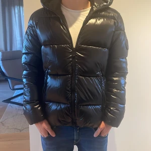 Svart pufferjacka från Save The Duck - Säljer en svart, glansig pufferjacka från Save The Duck med huva och dragkedja. Jackan är i nyskick och är bara använd ett fåtal gånger. Perfekt för kalla dagar. Pris går att diskutera 