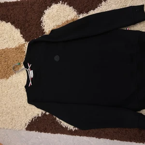 Svart sweatshirt från Moncler - Säljer en stilren svart sweatshirt från Moncler i storlek S. Tröjan har rund halsringning, diskret Moncler-logga på bröstet och klassiska ränder i kragen. Perfekt för dig som gillar enkel och snygg design.