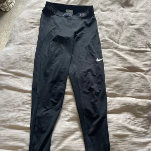 Svarta Nike Dri-Fit leggings S - Svarta leggings från Nike med Dri-Fit-teknologi och elastisk midja med Nike-logga. Tight passform och diskret vitt märke på benet. Perfekta för träning! 