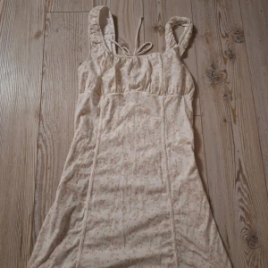 Blommig kortklänning från H&M - Helt ny supersöt kortklänning från H&M Köpt för 330kr. Den krämvit med små rosa blommor och gröna blad. Klänningen har breda axelband, söt knytning framtill och en lätt figurnära passform. Perfekt för varma dagar och somriga vibes!