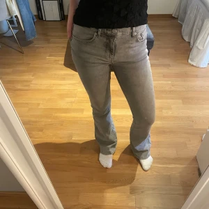 Grå bootcut jeans med hög midja - Snygga grå jeans med bootcut-modell och hög midja. Jeansen har klassisk femficksdesign, dragkedja och knapp framtill. Materialet är mjukt och stretchigt jeans, perfekt för en avslappnad men trendig look.