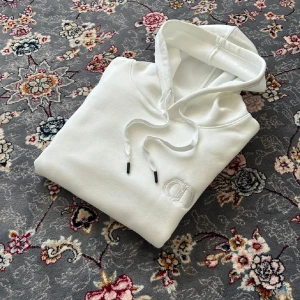 Vit hoodie från CD - Säljer en clean vit hoodie med broderad CD-logga på bröstet. Tröjan har huva med snörning och en stor magficka. Mjuk bomullskänsla och klassisk passform, perfekt för en chill och stilren look.
