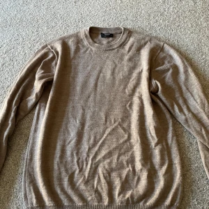 Beige stickad tröja från Magasin - En stilren beige stickad tröja från Magasin, tillverkad i Italien. Tröjan har rund halsringning och långa ärmar, perfekt för lager-på-lager. Enkel och klassisk design som funkar till det mesta. Materialet är mjukt och skönt mot huden.